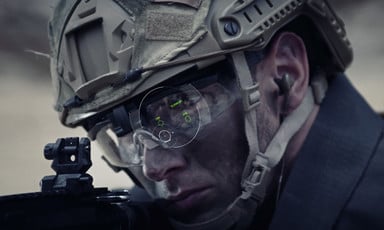 Soldier wearing helmet looks at gun. 