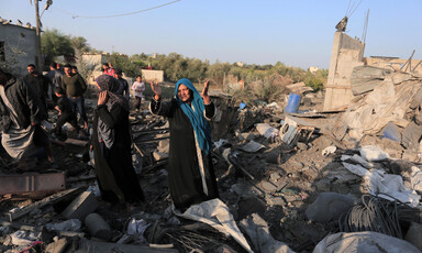 Woman throws her hands in the air while standing on rubble