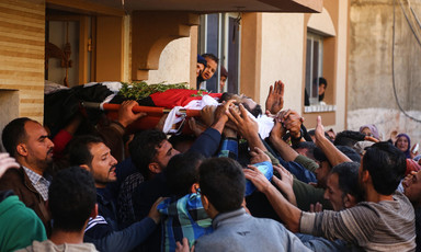 Body sheathed in flag is carried out of home by crowd of men