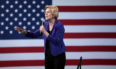 A woman with a microphone in front of American flag