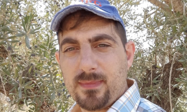 Man wears a cap standing in front of olive branches