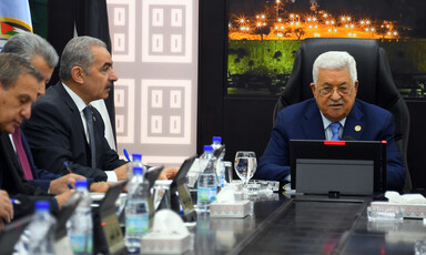 Man sits at desk, surrounded by other men 