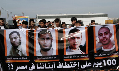 People hold up posters with the pictures of four men. 