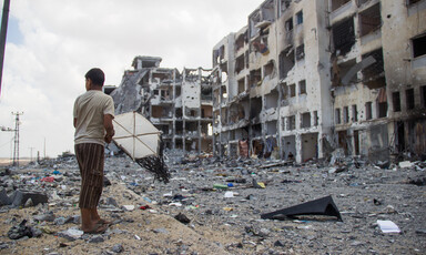 Boy holds kite in front of bombed-out multi-story buildings