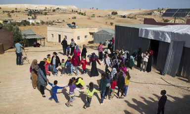 People dance in a circle near building structures 