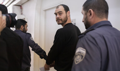 Man walks behind police officer to whom he is handcuffed.