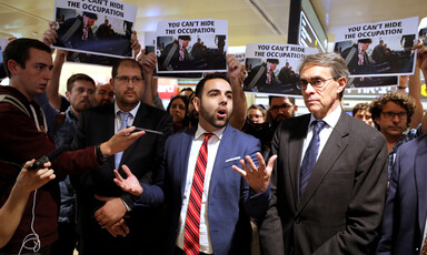 Man turns palms of his hands upwards as people around him hold placards