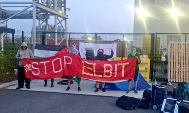 Masked protesters with a large banner block a factory gate