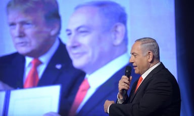Benjamin Netanyahu speaks into a microphone in front of a picture of himself with US president Donald Trump