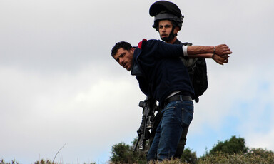 A soldier restrains a man who is in handcuffs