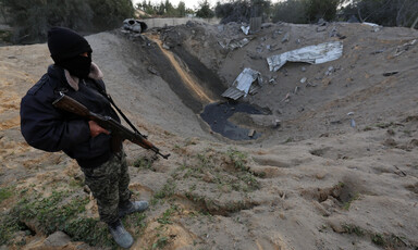 Masked man holding gun stands near sandy crater