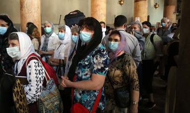 People wear paper masks over their mouths while standing next to pillars