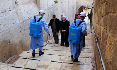 Men wearing protective clothing use backpack sprayers in alley