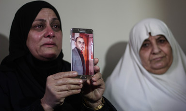 Two women cry, one holds up a picture of a man displayed on a phone