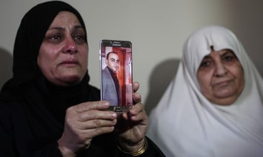 Two women cry, one holds up a picture of a man displayed on a phone