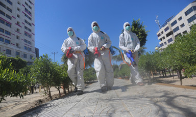 Three men in hazmat suits carrying spraying equipment