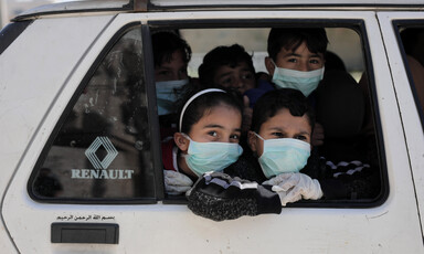 Children wearing face masks look out of vehicle window 