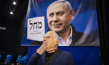 Man wearing a mask stands in front of Netanyahu banner