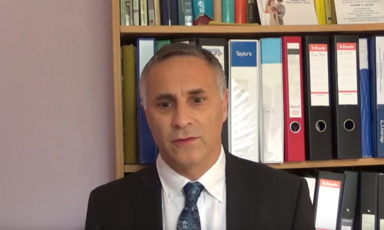 A man in a suit stands before a book shelf