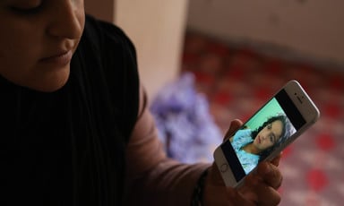 A woman holds a phone showing a picture of herself as a young girl