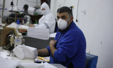 People wearing protective gear work at sewing machines