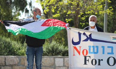 Two men wearing face masks hold Palestine flag and banner