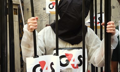 A protester wears a hood behind bars