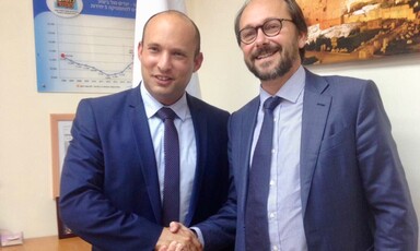 Two men in suits smile and shake hands