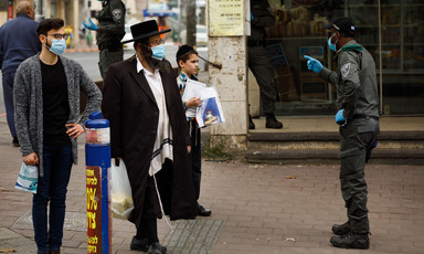 Israeli policeman in face mask gestures at two men in masks and a boy