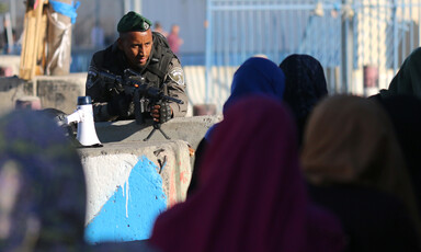 Soldier pointing rifle leans over women at checkpoint