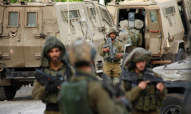 Heavily armed soldiers stand in front of military vehicles