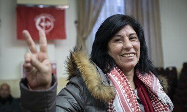 Smiling woman seen from chest up makes V for victory sign with her hand