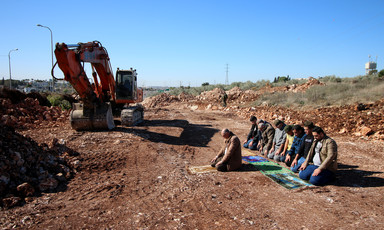 Men pray near construction equipment