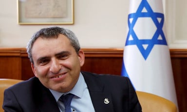 Smiling man seen from chest up sits in front of Israeli flag