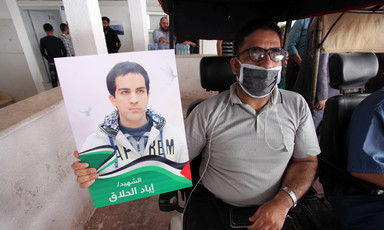 Man in wheelchair holds poster of Iyad Hallaq