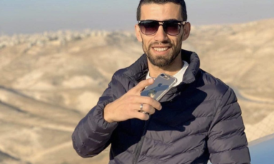 Man smiles and holds phone against backdrop of mountains
