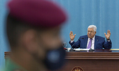 Mahmoud Abbas gestures behind the blurred profile of a Palestinian security officer