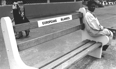 Man sits on edge of bench that says Europeans Only