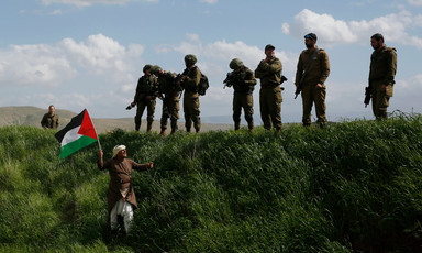 A man waves a Palestinian flag in front of a group of Israeli soldiers