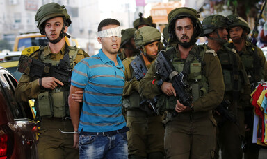 Soldiers restrain a blindfolded youth