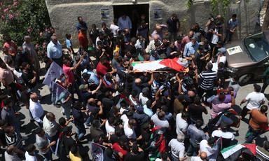 Crowd carries body on stretcher wrapped in Palestine flag