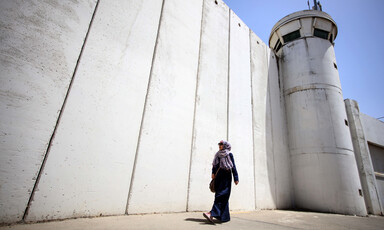 Woman walks past wall and tower 