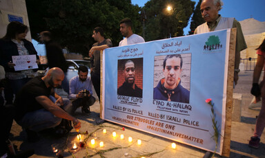 Man lights candles before banner with two portraits of men