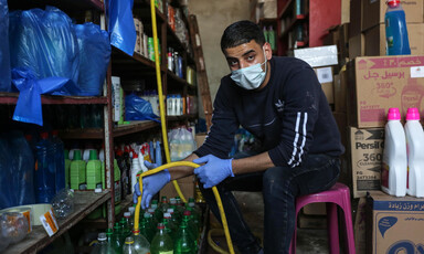 A young man wearing a face mask fills a plastic bottle from a yellow hose