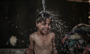 A boy smiles as water is poured over his head