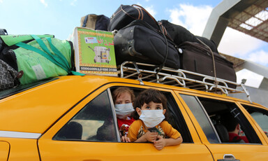 Two children wearing masks look out a car window 