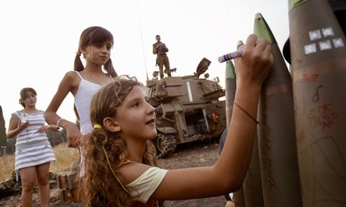 Smiling girl writes on munition as others look on
