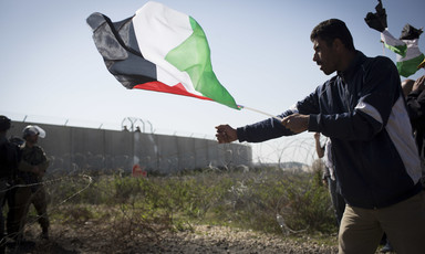 Man holding Palestine flag grabs barbed wire fence near Israeli soldiers