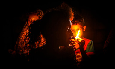 Girl stands in front of boy holding candle