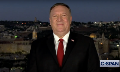 Man speaks to camera with evening cityscape behind him